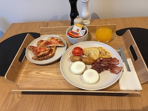 A breakfast tray with toast, eggs, bacon, sausages, tomatoes, and a glass of orange juice. - The Stables Motel (Bulls)