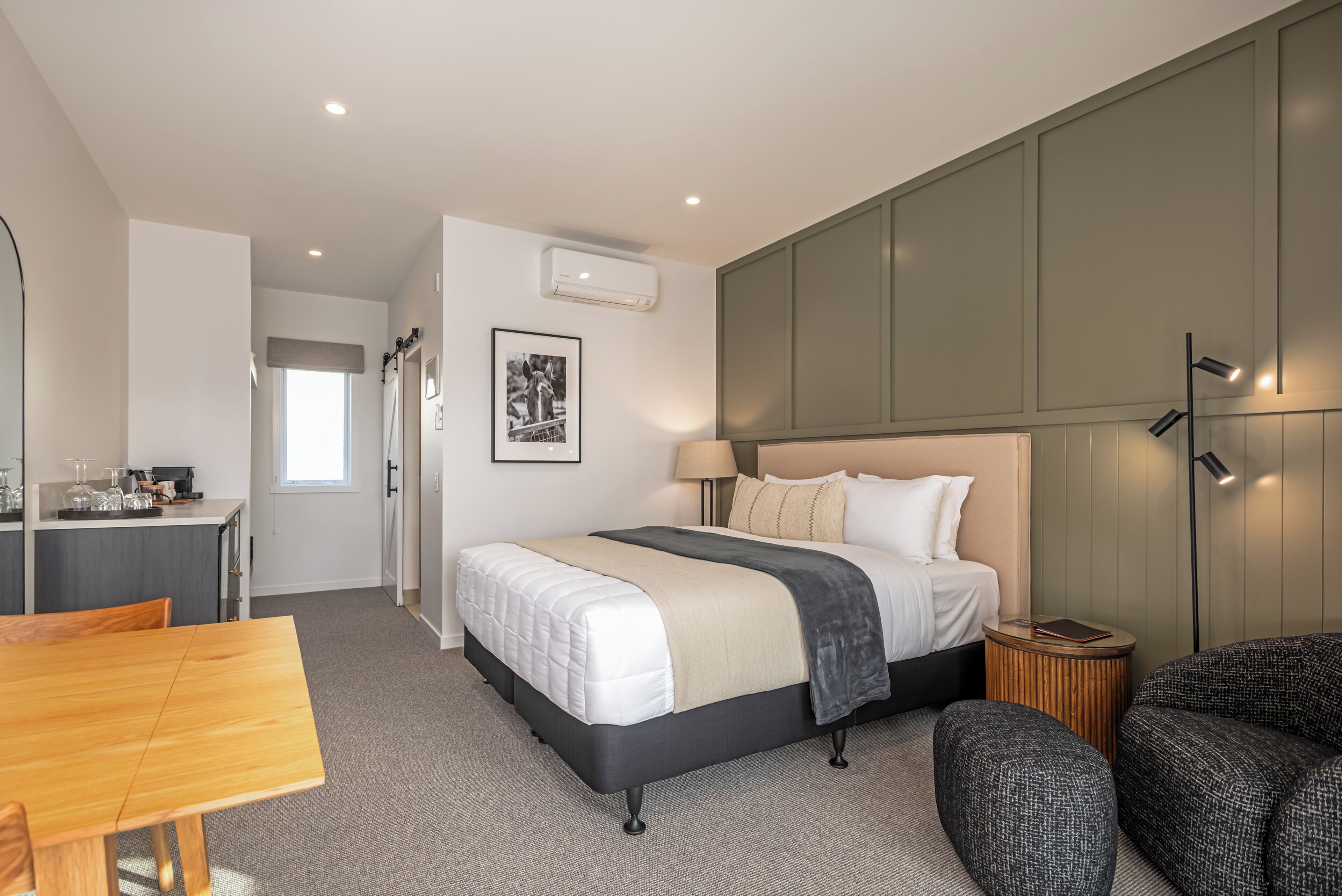 A modern hotel room with a bed, bedside table, lamp, and a view of the hallway.