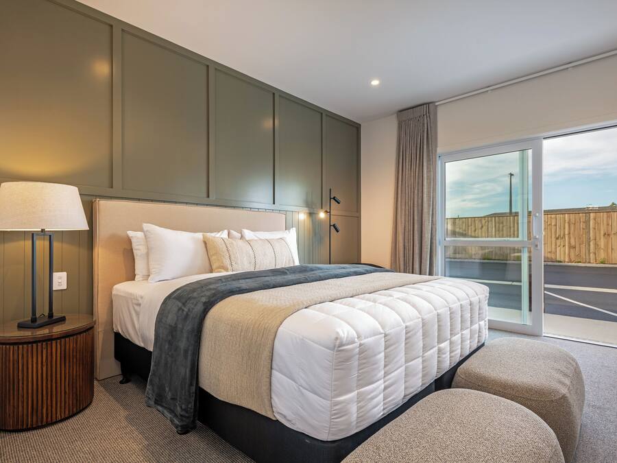 A modern hotel room with a large bed, a bedside table with a lamp, and a view of the outside.