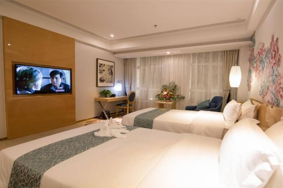Habitación de hotel con dos camas, un escritorio con silla, un televisor y un adorno en la pared.