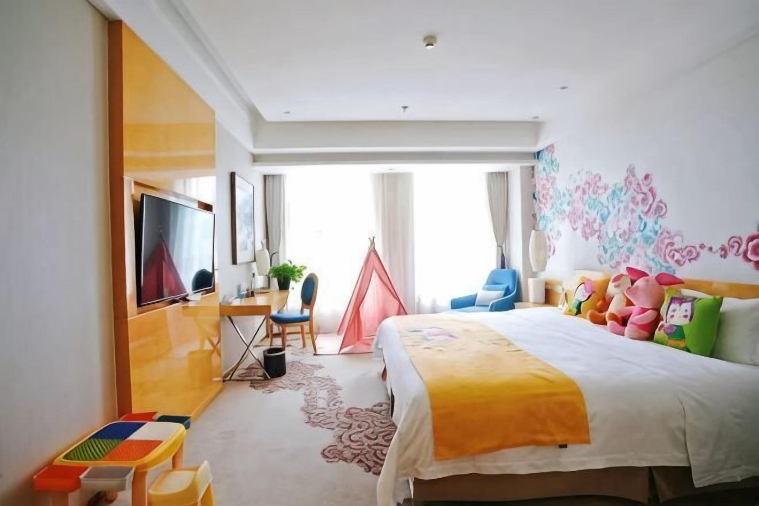 Habitación de hotel con cama, escritorio, silla, televisor, ventana y puerta.