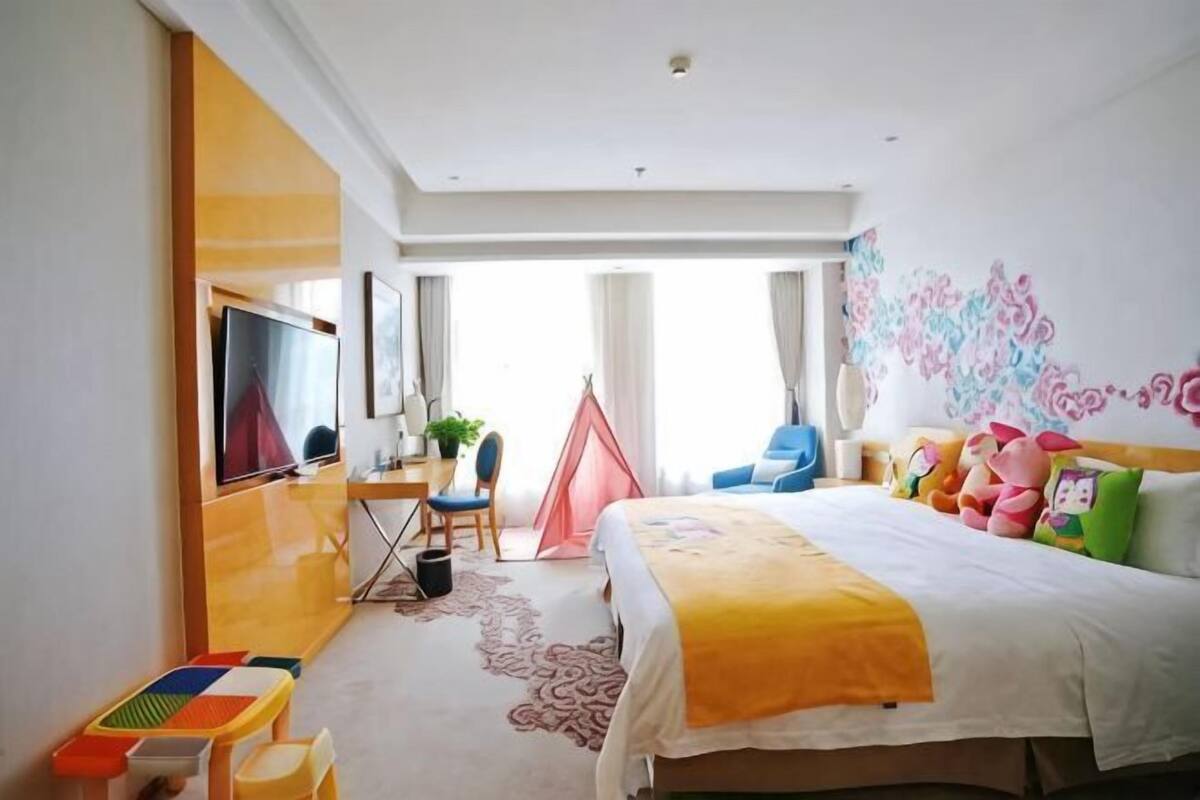 Habitación de hotel con cama, escritorio, silla, televisor, ventana y puerta.