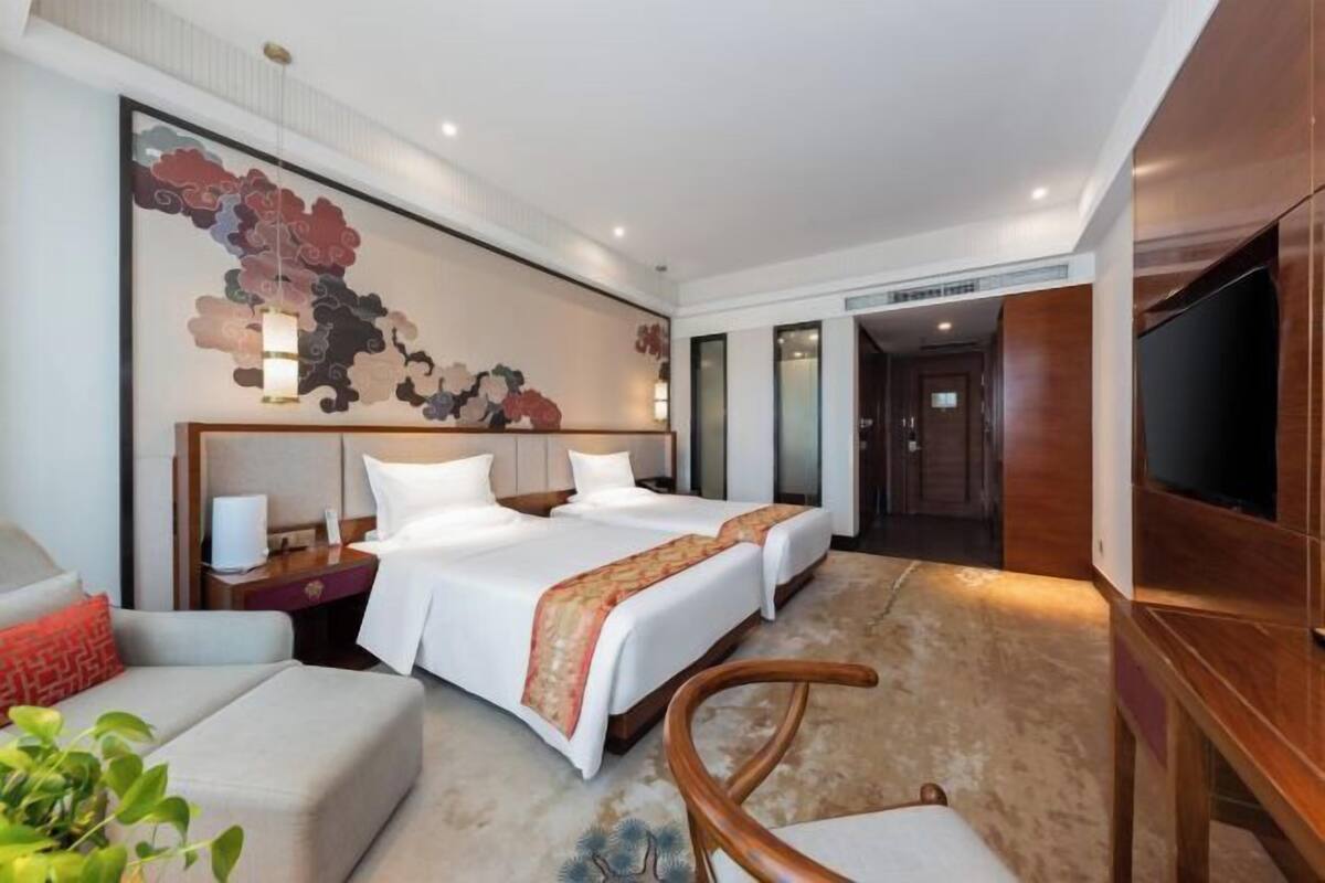 Una habitación de hotel con una cama grande, un escritorio, una silla, un televisor y un adorno en la pared.