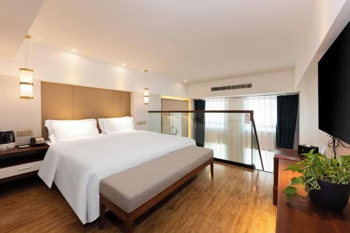 Una habitación de hotel moderna con una cama grande, mesitas de noche, un televisor y una planta en maceta.