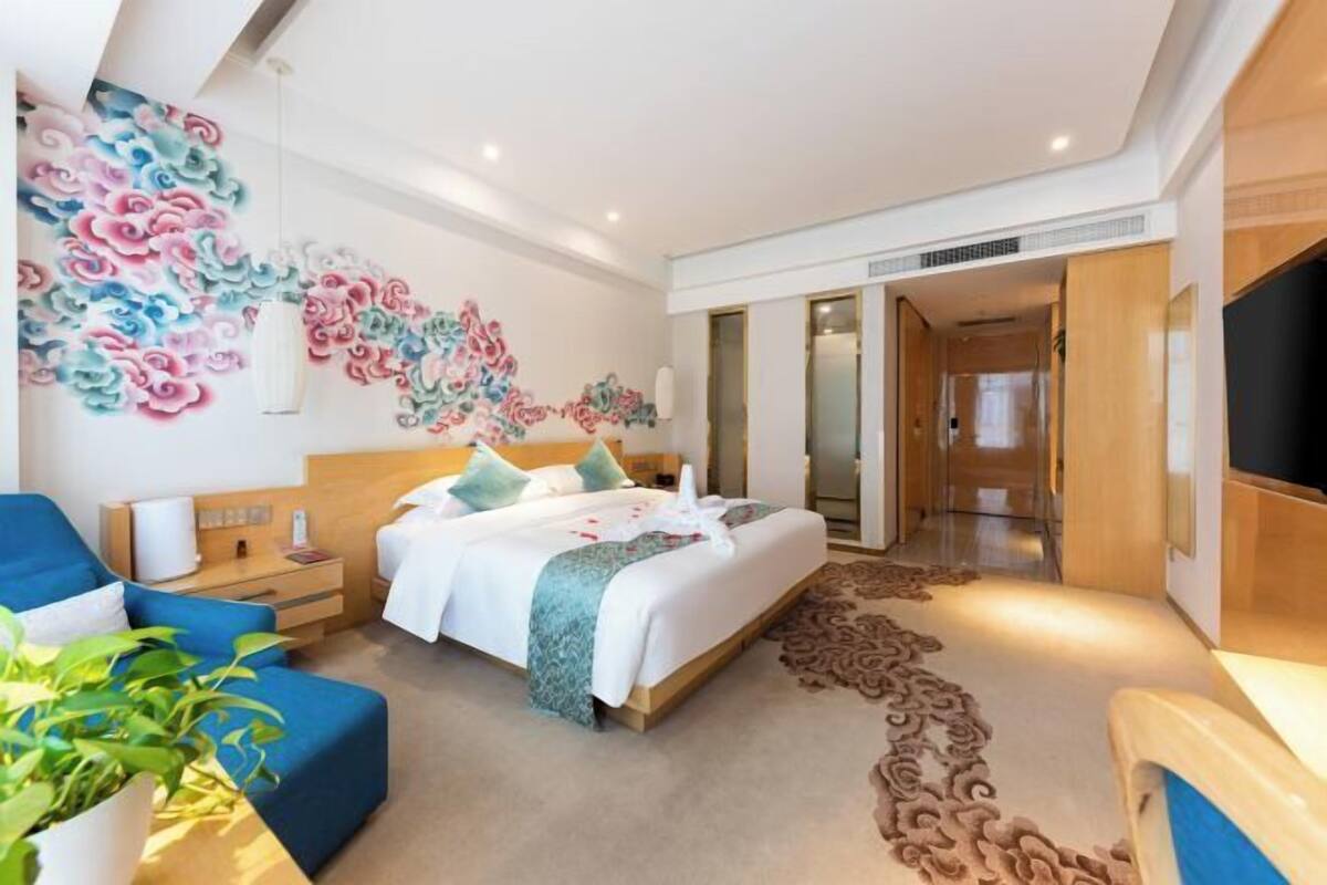 Una habitación de hotel con una cama, un sillón azul, una pared con un mural floral y un televisor.