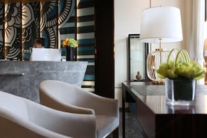 Un vestíbulo de hotel moderno con un mostrador de recepción de mármol, una gran obra de arte abstracta en la pared, una zona de estar con sillas y una lámpara sobre una mesa.