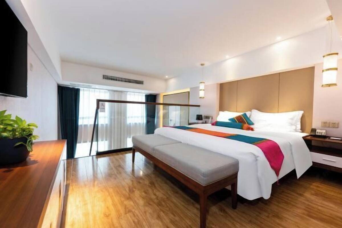 Una habitación de hotel moderna con una cama grande, un banco, un televisor y una planta en maceta.