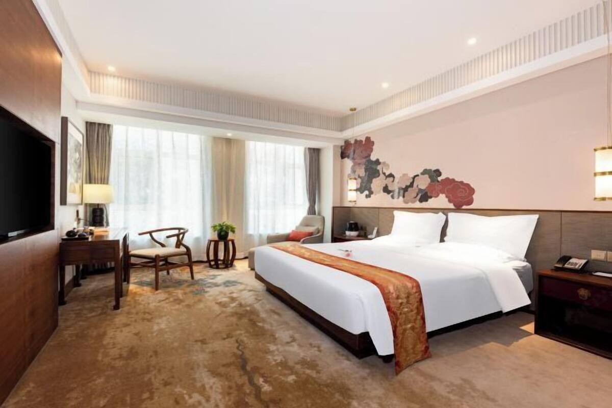 Habitación de hotel con una cama grande, un escritorio, una silla, un televisor y una obra de arte en la pared.