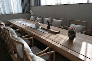 Un salón de conferencias con una larga mesa de madera, sillas acolchadas y un jarrón con flores.