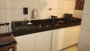Una cocina con encimera negra, armarios blancos, un lavamanos, una cafetera y una estantería con una botella y un jarrón.