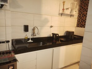 Eine Küche mit schwarzem Arbeitsplatz, weißen Schränken, einer Spüle, einer Kaffeemaschine und einem Regal mit einer Flasche und einer Vase.