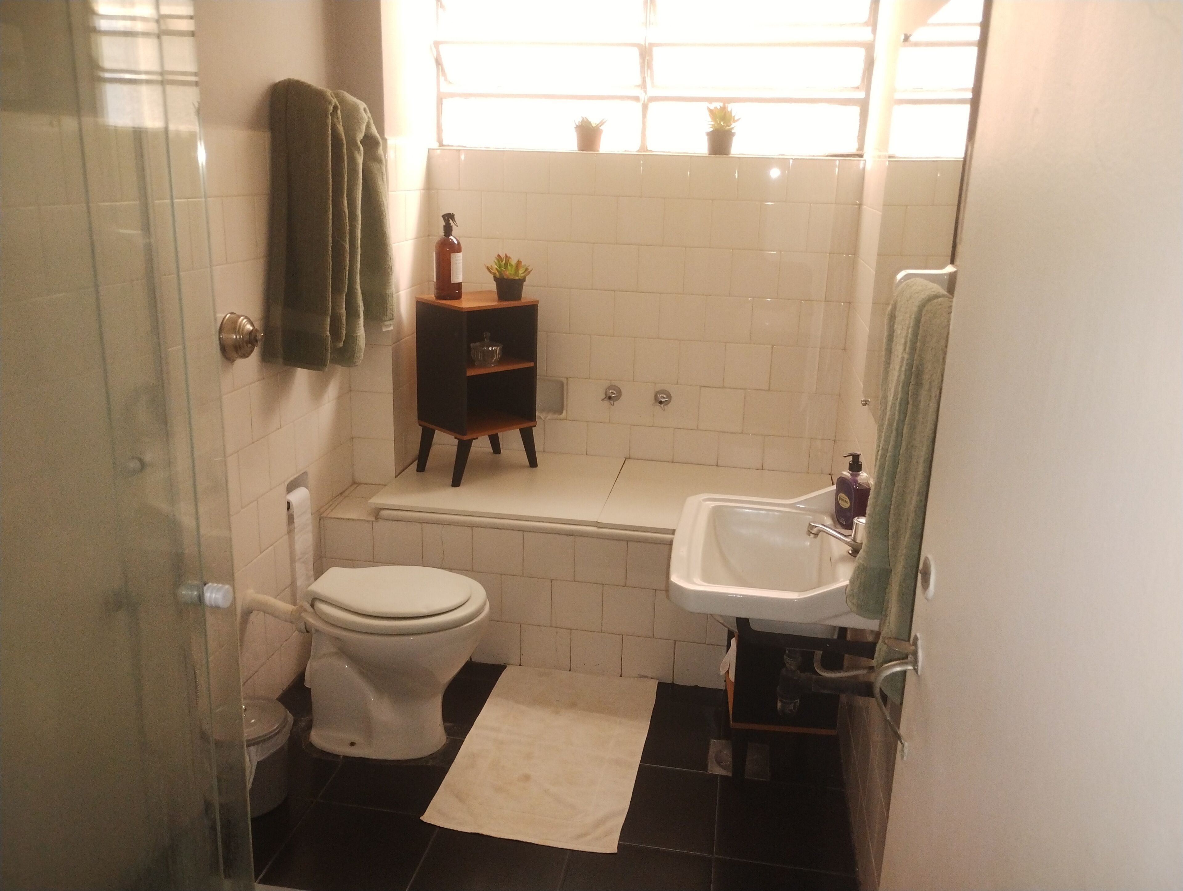 Et badeværelse med toilet, vask, badekar og en lille hylde med en plante.