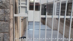 Una entrada protegida por una verja de metal, un muro de piedra y un edificio con techo de tejas al fondo.