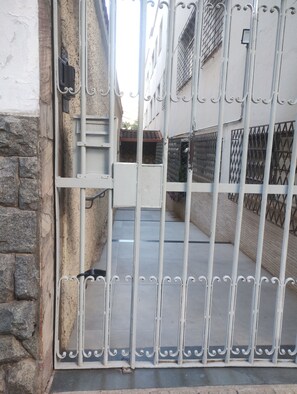 Ein verschlossener Eingang mit einem Metallgitter, einer Steinmauer und einem Gebäude mit einem Ziegeldach im Hintergrund.