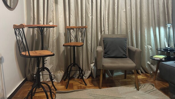 Una habitación con una silla, dos mesitas, una lámpara y una cortina.