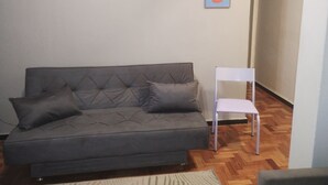 Un sofá gris con dos cojines, una silla blanca y un pequeño cuadro en la pared.