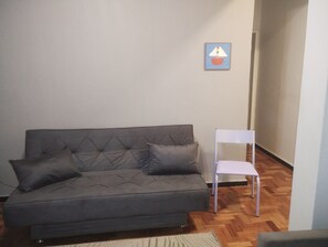 Ein graues Sofa mit zwei Kissen, ein weißer Sessel und ein kleines gerahmtes Bild an der Wand.