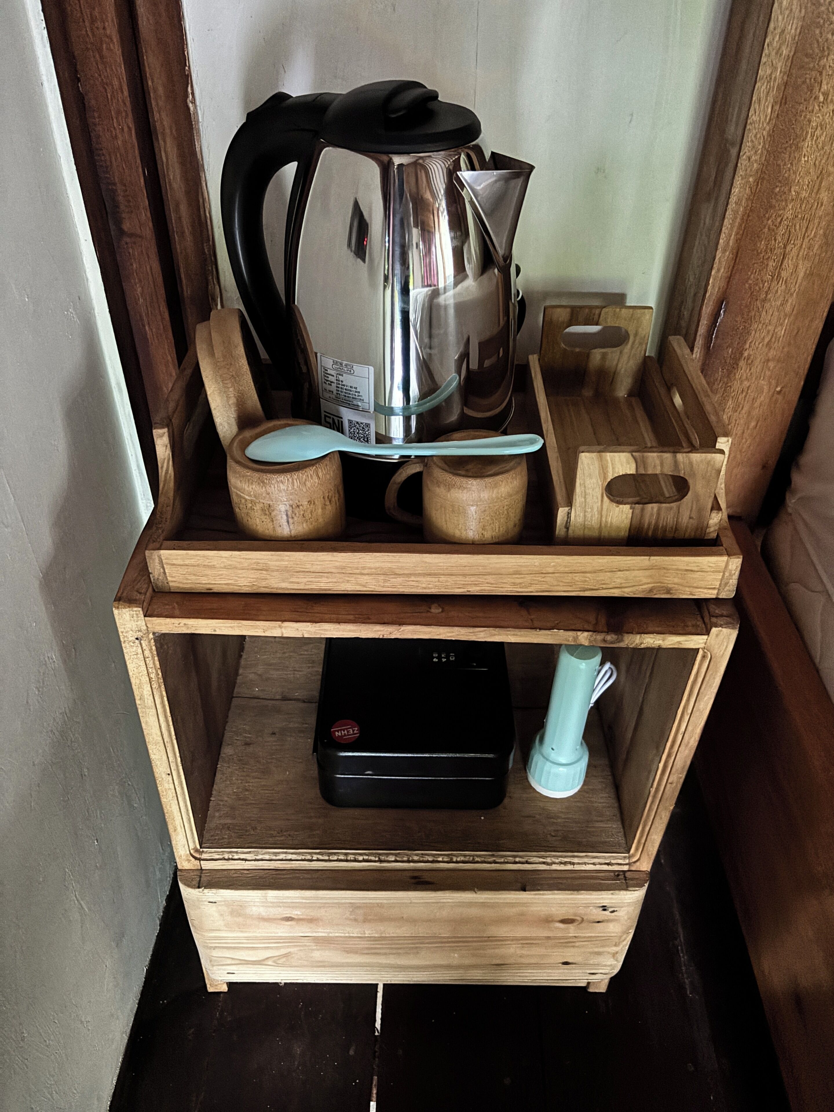 A wooden shelf with a kettle, a coffee pot, and a small appliance.