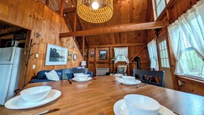 Interior de uma cabana de madeira com uma mesa de jantar posta para quatro pessoas, um sofá e um lustre.