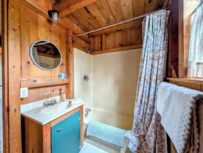 Ein Badezimmer einer Holzhütte mit Waschbecken, Spiegel, Dusche und Handtuchhalter.