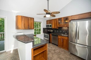 A kitchen with wooden cabinets, stainless steel appliances, a granite countertop, and a ceiling fan.