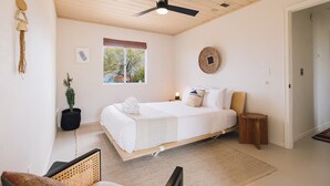 Ein Schlafzimmer mit Bett, Deckenventilator, Fenster und Zimmerpflanze.