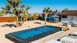 Ein Schwimmbecken mit einer erhöhten Liegeinsel, umgeben von Liegestühlen und einer Terrassenanlage.