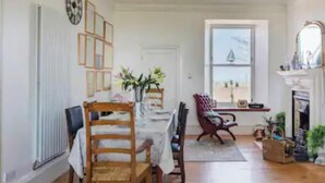 A dining area with a table, chairs, a vase with flowers, a window with a view, and a fireplace. - 4 Bed House - Sleeps 10 - Pets - Garden - Parking (Banff)
