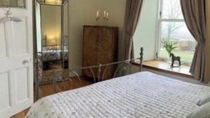 A bedroom with a bed, a dresser, a mirror, and a window with curtains. - 4 Bed House - Sleeps 10 - Pets - Garden - Parking (Banff)