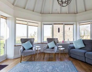 A spacious room with a high ceiling, large windows, a grey sofa, two armchairs, a small table, and a patterned rug. - 4 Bed House - Sleeps 10 - Pets - Garden - Parking (Banff)
