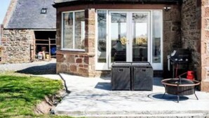 A stone building with a tiled roof, a glass door, and a small outdoor seating area with a grill. - 4 Bed House - Sleeps 10 - Pets - Garden - Parking (Banff)
