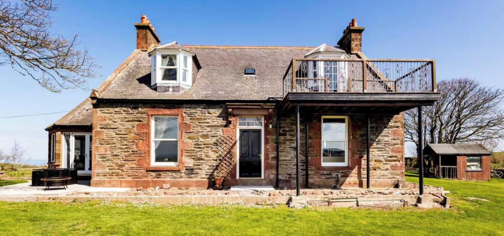 A stone house with a balcony, a front door, and a small attached shed.