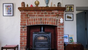 Una chimenea de ladrillo con una estufa negra, una pequeña mesa de madera y un banco.