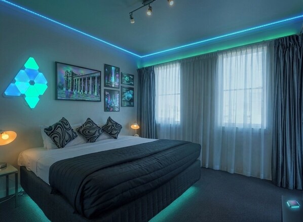 A modern hotel room with a large bed, a geometric light fixture, framed pictures, and a view of the outdoors. - High Tech Living || Walking Distance City (Carlton)