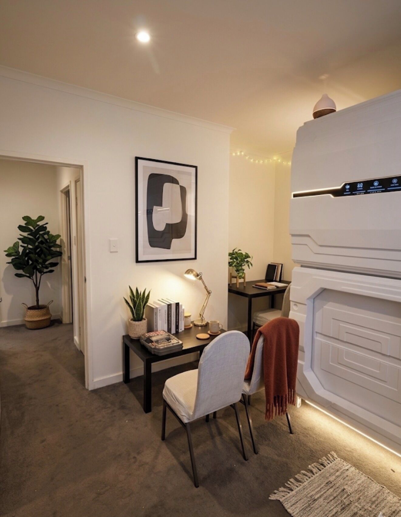 Een moderne woonkamer met een open haard, een bureau met een lamp en een kunstwerk in een lijst aan de muur.