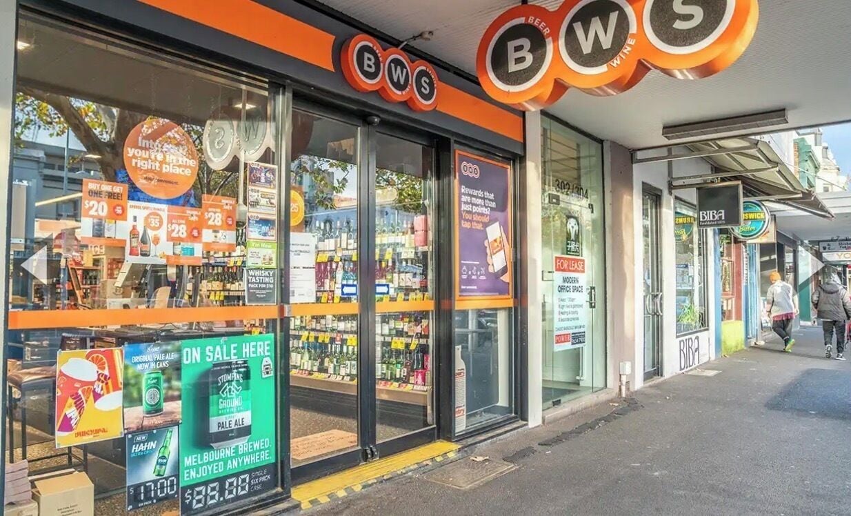 A storefront with a sign reading 'BWS' and various promotional signs for products.