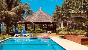 A swimming pool with lounge chairs, a flamingo float, and a thatched-roof structure.