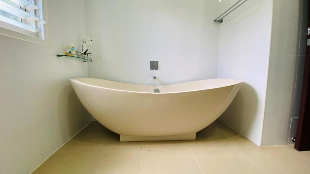 A modern bathroom with a freestanding bathtub, a glass shelf with toiletries, and a visible light switch on the wall.
