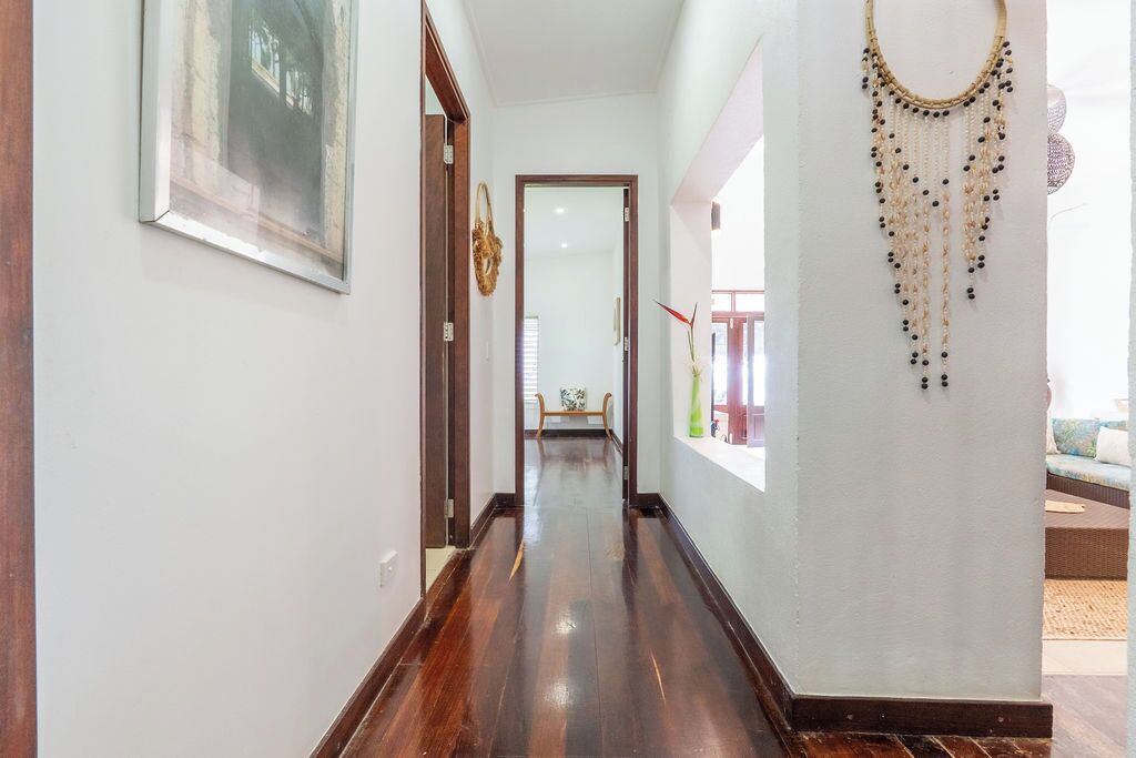 Un couloir avec un plancher en bois, un tableau encadré sur le côté gauche et un objet décoratif sur le côté droit.