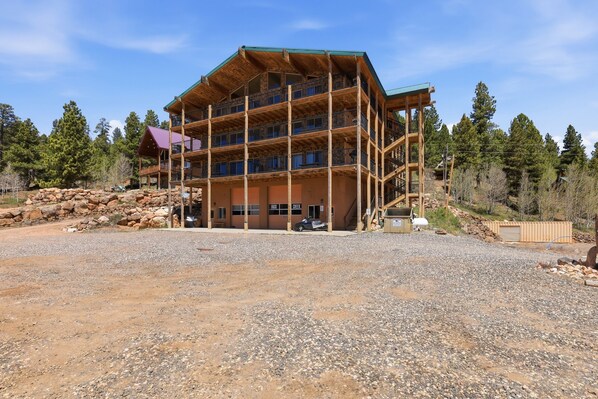 A multi-story wooden building with balconies, a gravel driveway, and surrounding trees.