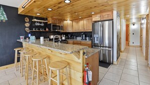 Eine Küche mit Holzausstattung, einer Arbeitsplatte aus Granit, Edelstahlgeräten und einer Bar mit Hockern.