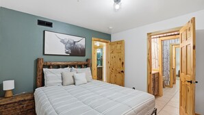Ein Schlafzimmer mit einem Bett, einem Holz-Kopfstück, einem gerahmten Bild, einem Nachttisch und einer Holztür.