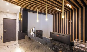 A reception area with a marble floor, a reception desk, a computer, and a wall with vertical wooden slats. - Mokpo Hotel The City (Mokpo)