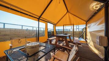 A tent with a table and chairs, a grill, and a view of a bridge.