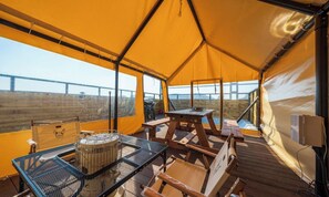 A tent with a table and chairs, a grill, and a view of a bridge.