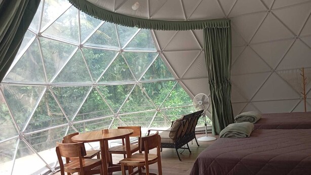 A room with a large window, a bed, a table with chairs, and a fan.