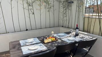 A dining table set outdoors with a bottle of wine, plates, cutlery, and a fruit platter.