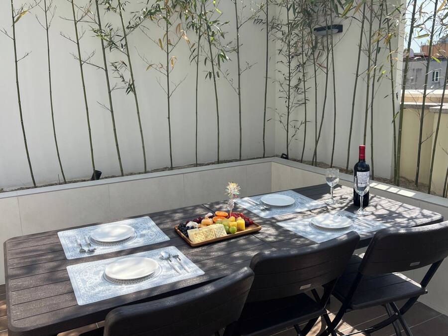 A dining table set outdoors with a bottle of wine, plates, cutlery, and a fruit platter.