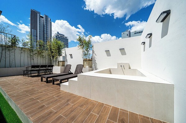 A rooftop patio with a wooden deck, outdoor seating, and a built-in hot tub.