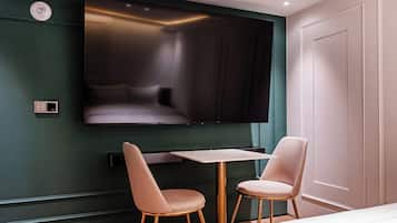 A modern hotel room with a flat-screen TV mounted on the wall, a small table, two chairs, and a bed.